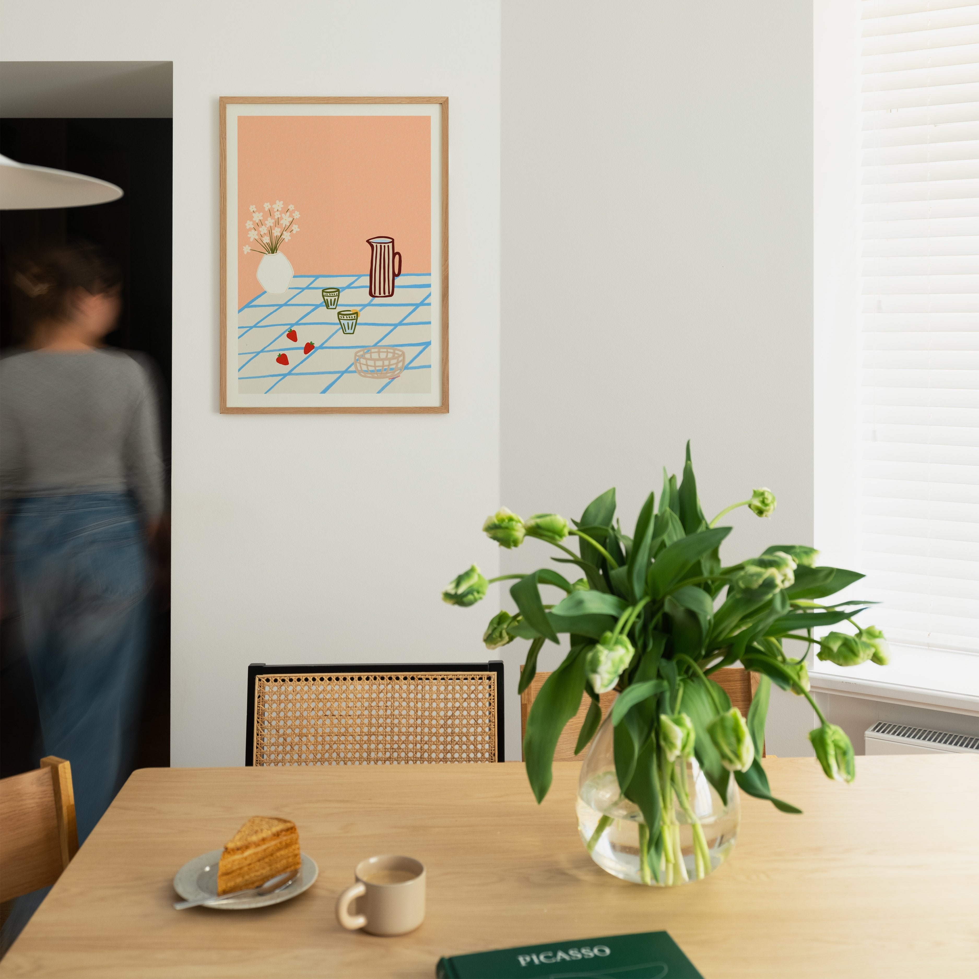 Featuring a striped pitcher, delicate flowers, two glasses, and fresh strawberries arranged on a blue-checkered tablecloth